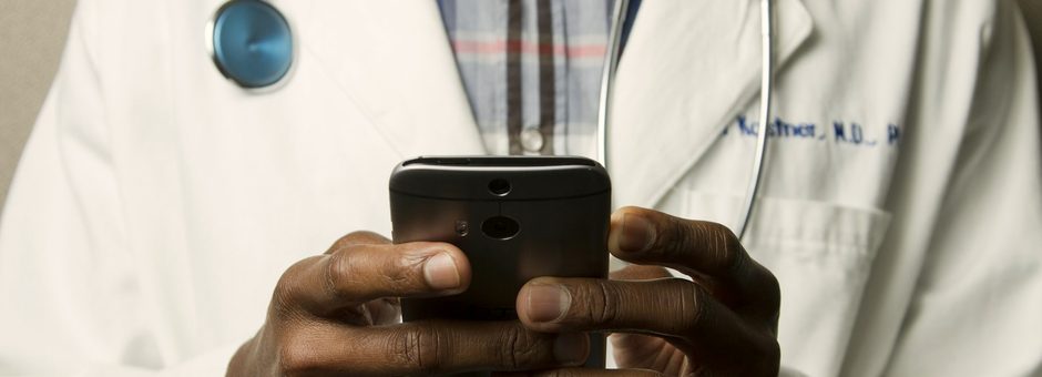 A clinician in a white coat reviewing member messages on a phone